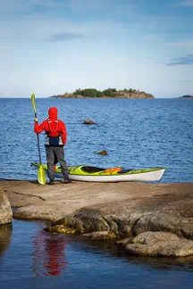a student standing on a rock , paddle in hand, preparing to kayak to a nearby ocean island